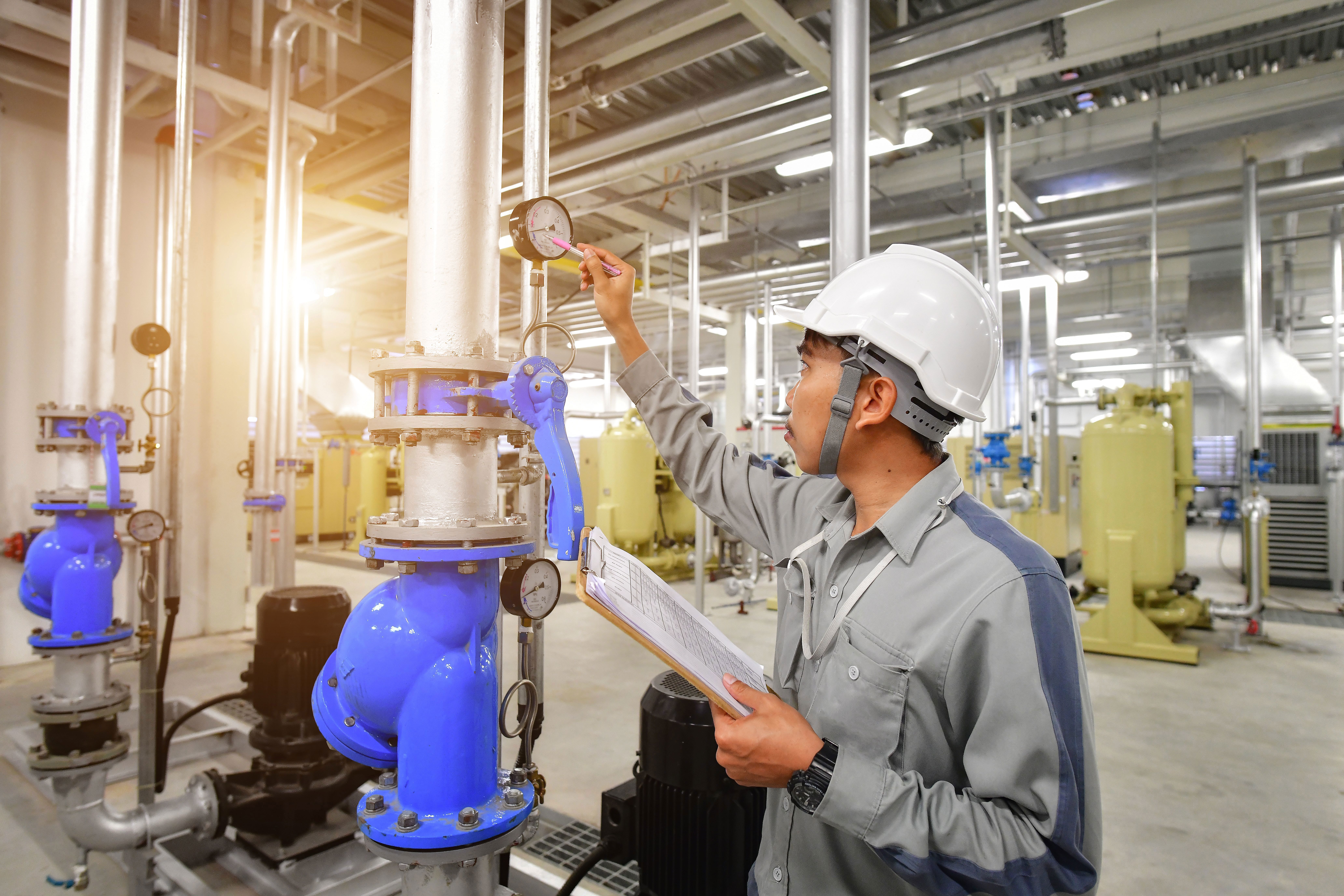 Tech Inspecting gauges on a large pipe in an industrial setting